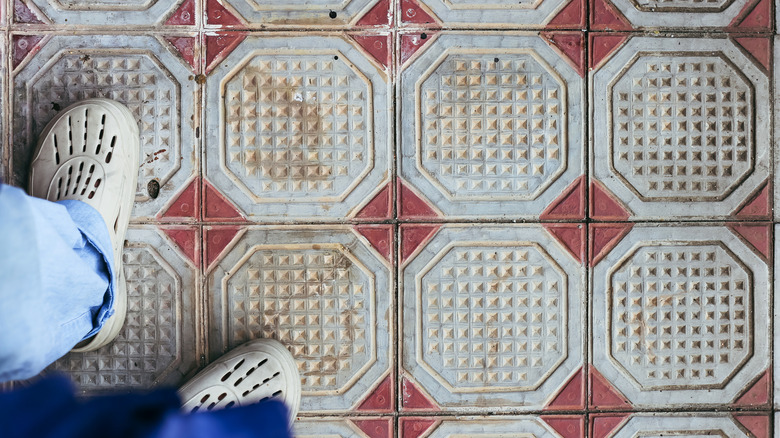 Person standing on old, damaged ceramic floor tiles