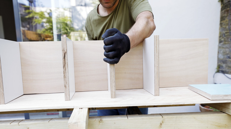 man putting light wood shelves together on work table