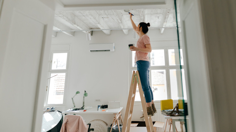 woman standing on ladder wile painting her ceiling