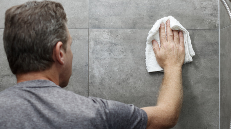 Man wiping gray stone shower tile with white towel