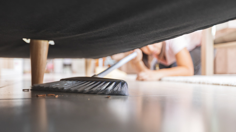 Woman sweeping crumbs underneath furniture