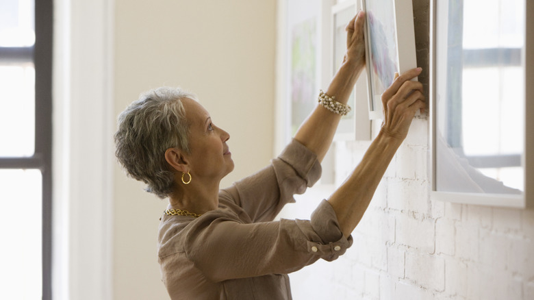 A woman hangs artwork on a wall