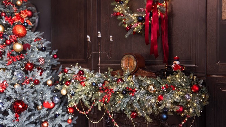 Large garland on mantel with berries, ornaments, and lights alongside matching tree and wreath