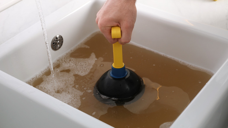 Person unclogging sink with plunger