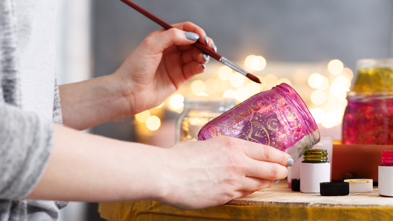 A person paints a glass jar pink for decor