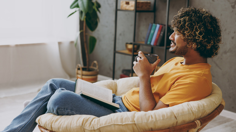 A young person relaxes in home library with a book in their lap