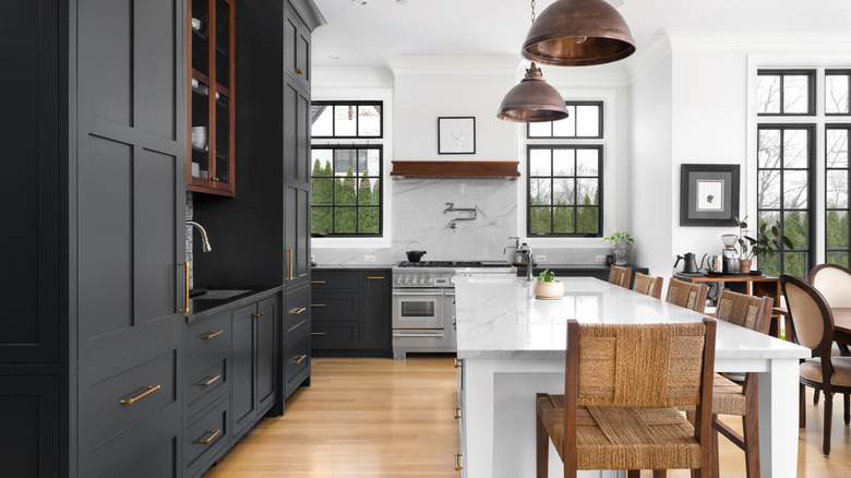 A kitchen with dark-colored cabinets, dome lights, and island with woven stools