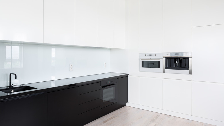 An all-white kitchen, featuring a glossy backsplash and black lower cabinets