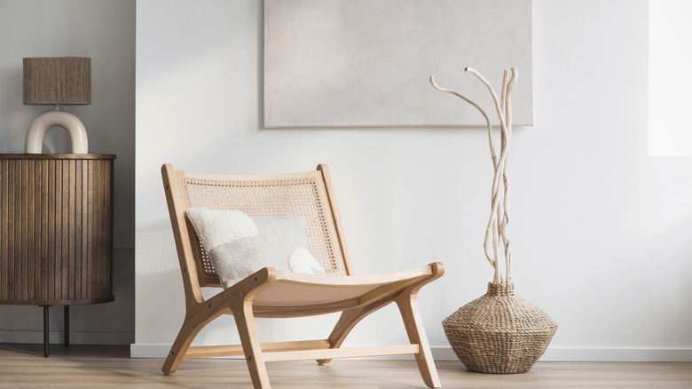 Minimalist space with woven rattan vase, wooden cabinet and wooden folding chair with pillow on it