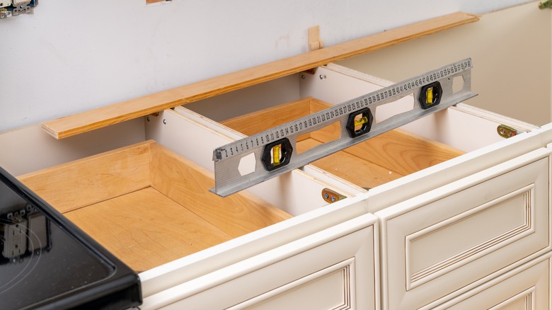 A leveler sits on top of unfinished kitchen cabinets