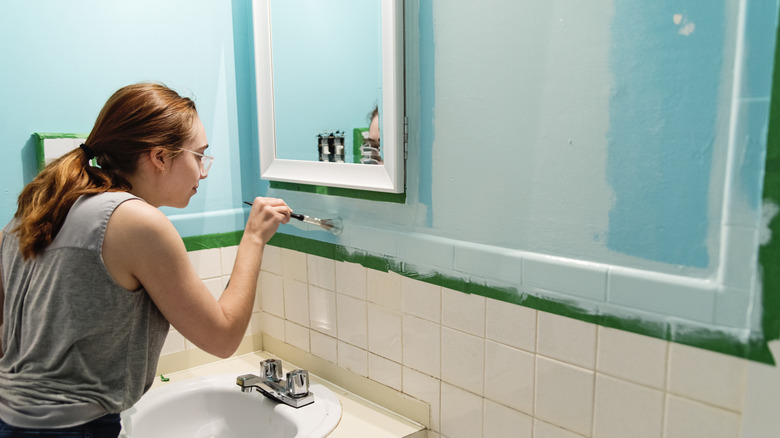 A woman paints a bathroom wall blue using a paintbrush