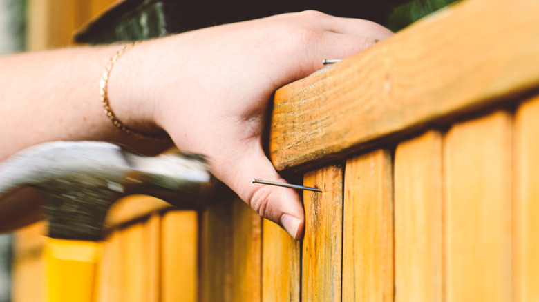 A man hammers a nail into a plank