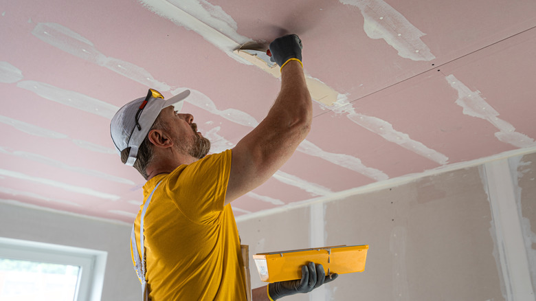 A repair person fixing the drywall on a ceiling