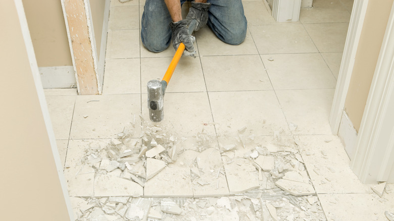 person breaking tile loose with sledgehammer