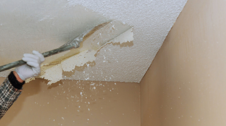 Person scraping away popcorn ceiling near corner