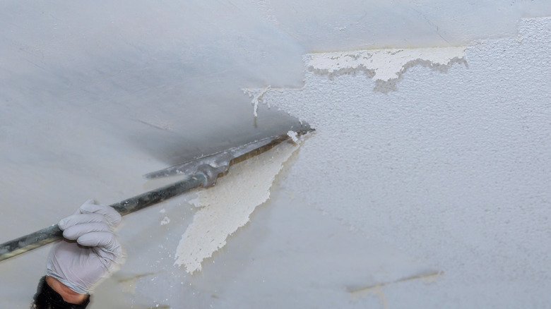 Person using scraper to remove popcorn ceiling section