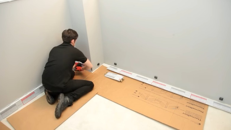 Handyman installing ThermaSkirt baseboards in room