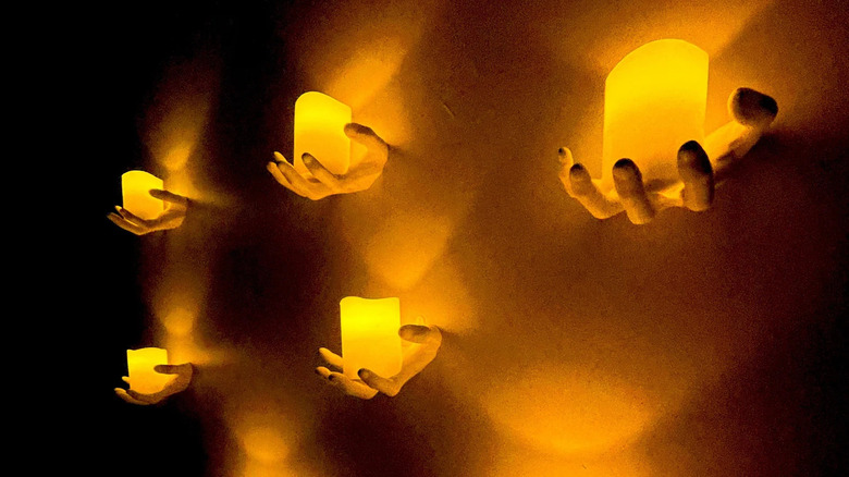 Hands holding candles on wall