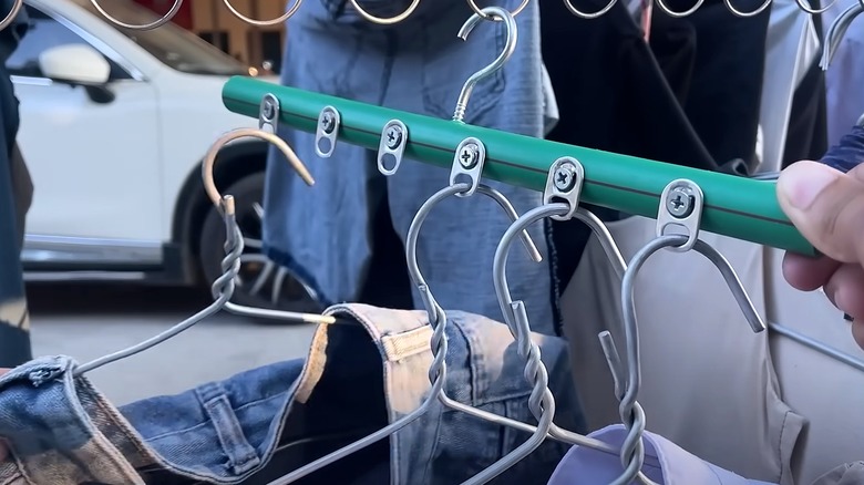 Person hanging shirts on a green broomstick with soda tabs turned into a multi hanger.