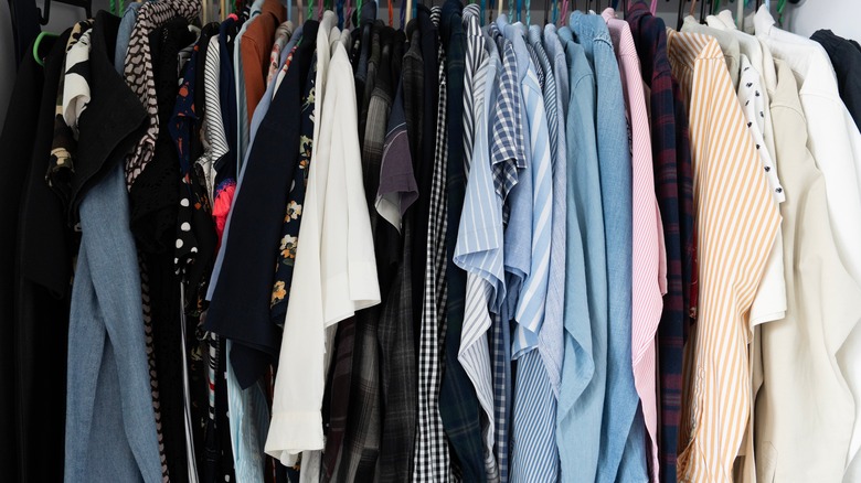 Shirts packed tightly to hang together in a closet that is in need of more hanging space.