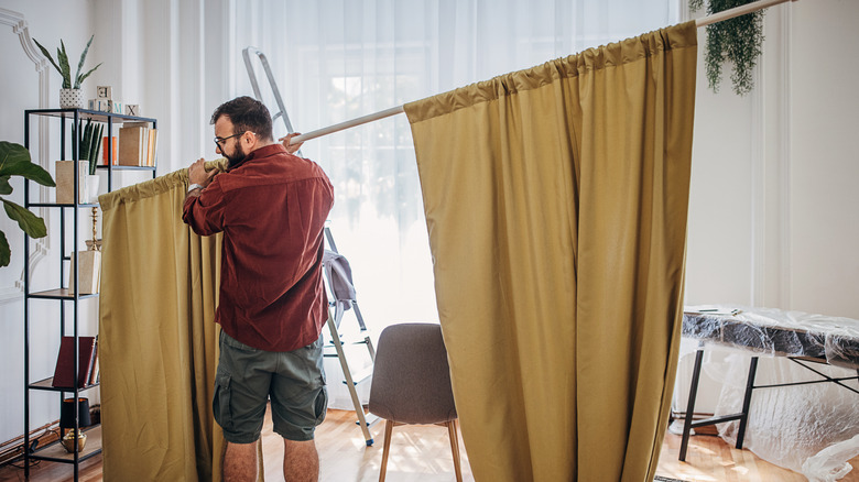 Man holding curtain rod with two khaki colored panels on either side