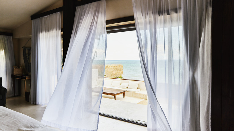 Sheer white curtains billowing into bedroom