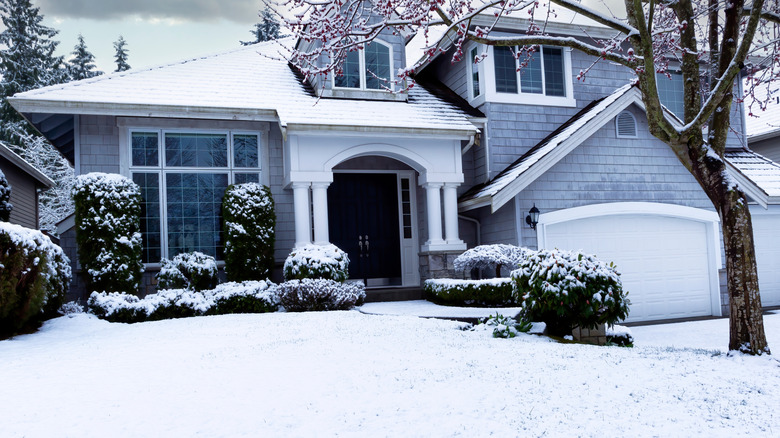 Snow covers a large front yard in front of a gray house