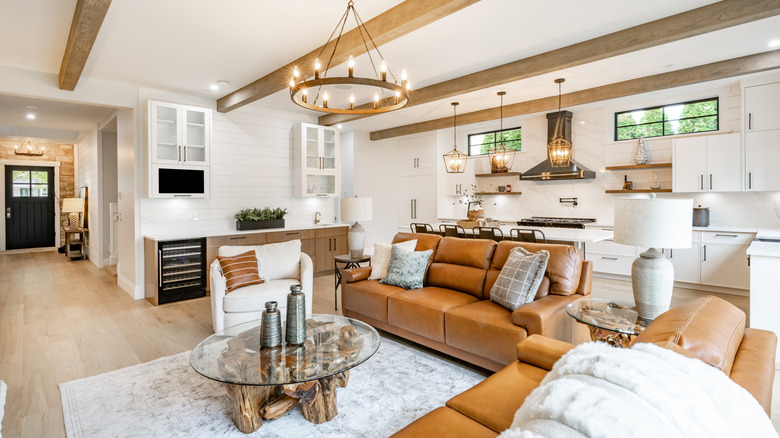 Living room in a modern home with leather couches, a coffee table with a natural wood base and glass top, metal and ceramic vases, with wood chandeliers, beams, and flooring