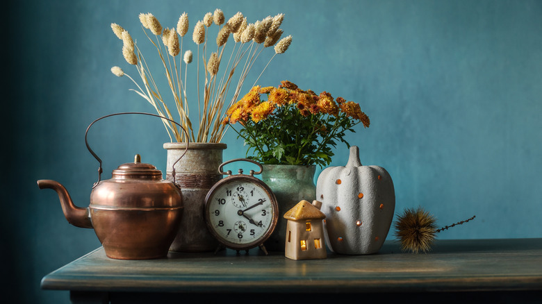 Antique copper kettle, ceramic vases with flowers in them, ceramic pumpkin decor, antique alarm clock, and small house decor