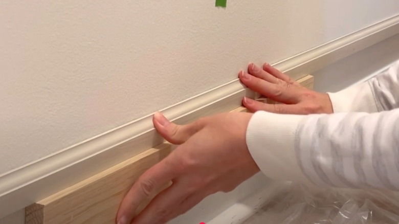 Woman holding lumber spacer between baseboard and new chair molding