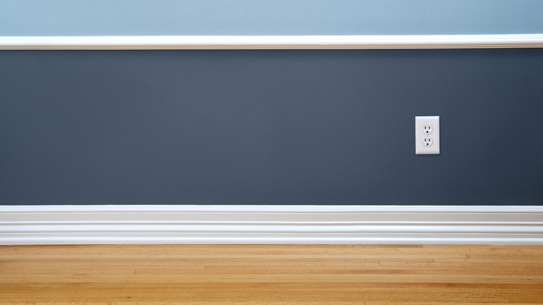 White baseboard on dark blue wall with outlet