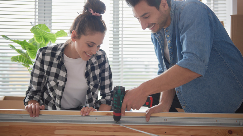 A couple installing a bed using an electric screwdriver.