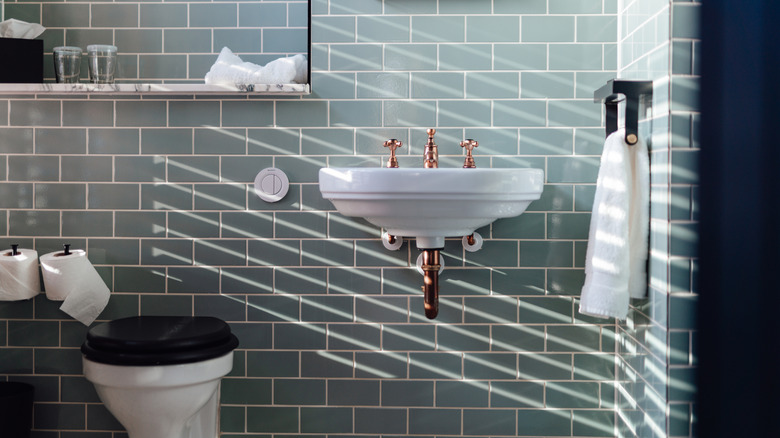 A stylish, light-dappled half bath with green tiles