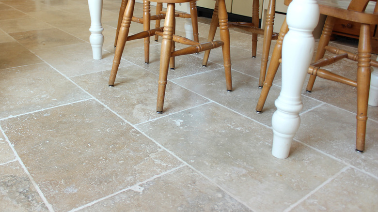 Travertine floors with white table and brown chair legs in frame.