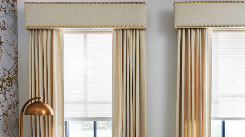 Two windows with cream-colored curtains and cornices