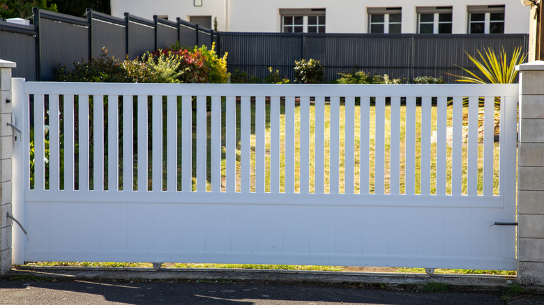 white aluminum gate with fence, shrubs, lawn, and house in background