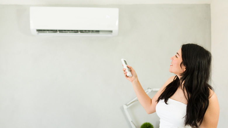 Woman using a remote to control a mini-split system hung on a wall