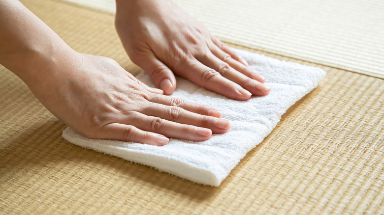 Hands cleaning a tatami mat with a white cloth