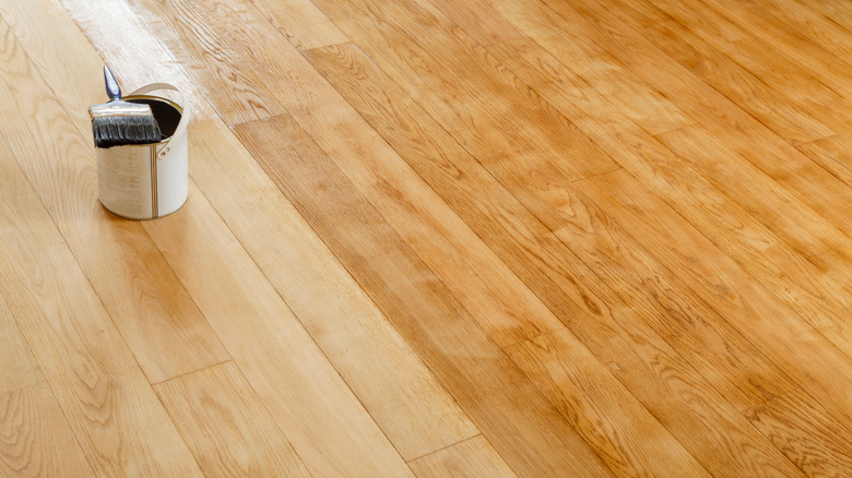 Solid hardwood floor with a tin of paint and a paint brush on it