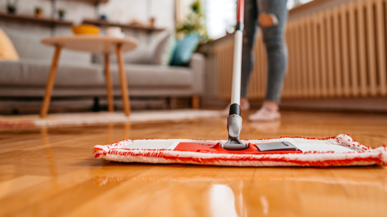 A person cleaning a wood floor with a cloth mop