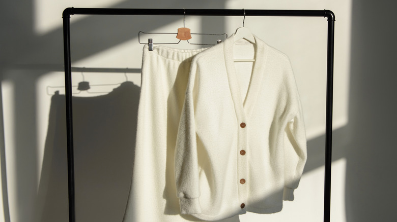 A woman's white sweater and skirt are hanging on metal hangers on a portable rack.