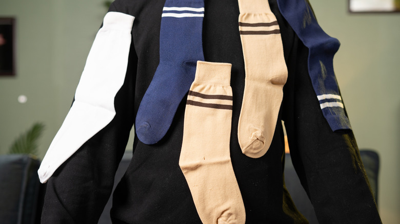 A person wearing a dark-colored sweater has five socks stuck to the back of it due to static cling.