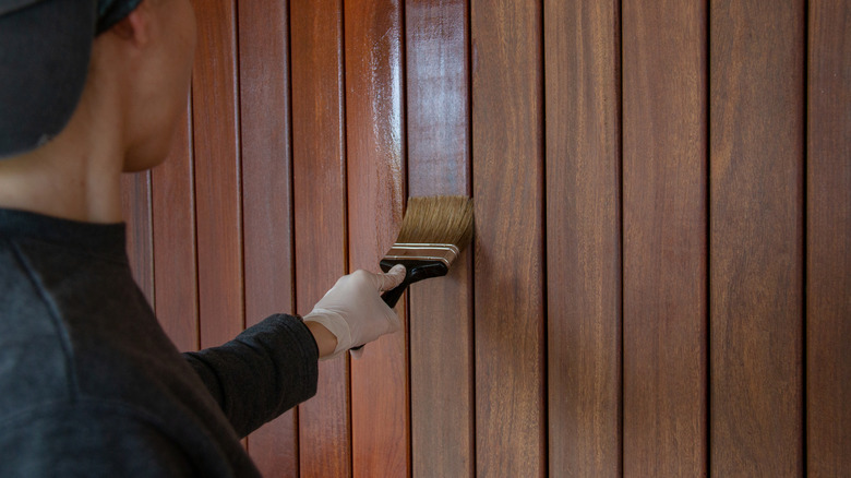 Person painting a finishing stain on wood paneled walls