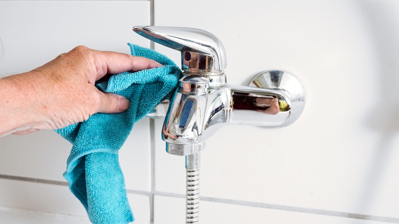 Person wiping a bath faucet with a blue microfiber cloth