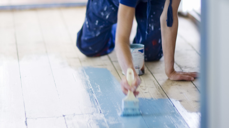 Woman painting hardwood floors in home with blue paint