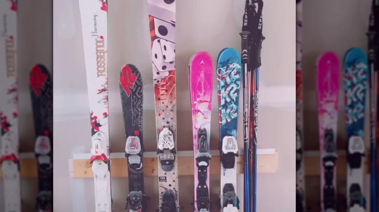 A line of skis are hung from their bindings on a backer board