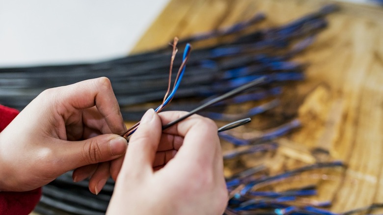 woman holding stripped and sheathed copper wires over bundle of black insulated wiring