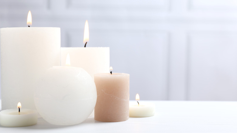 A collection of lit candles in different sizes and shapes on a table.