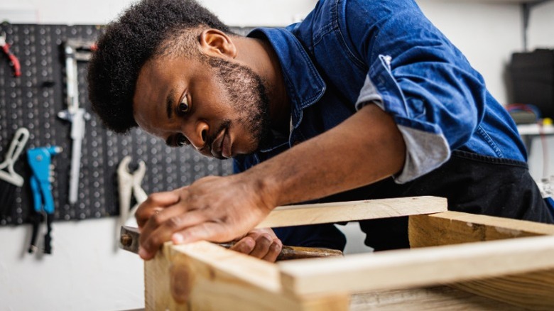 Man in a shop hammering wood boards together.