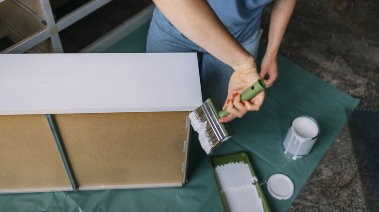 A person paints a cabinet white.